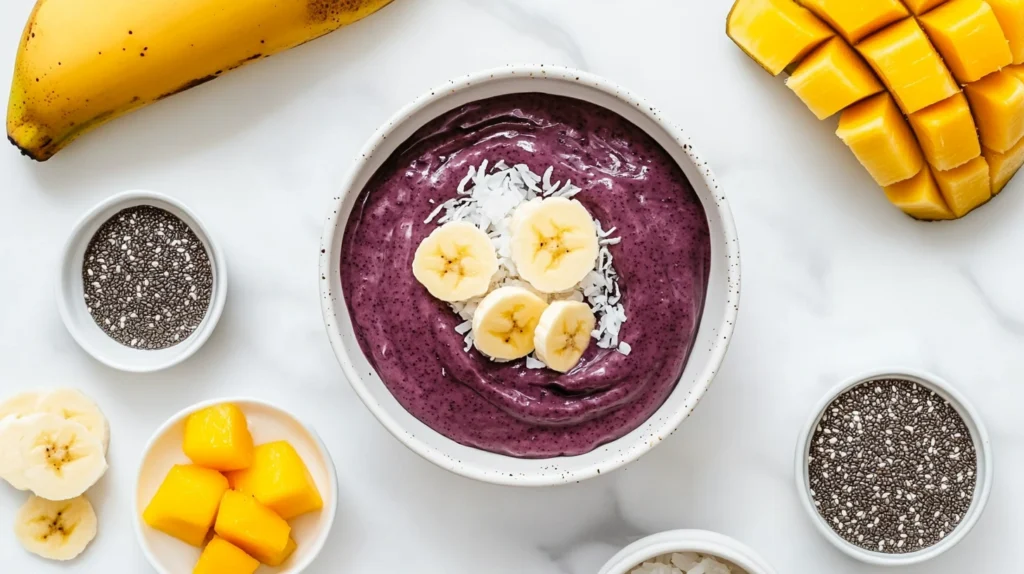 Ingredients for a tropical smoothie acai bowl, including acai puree, sliced fruits, and a jar of almond milk, arranged on a white countertop.